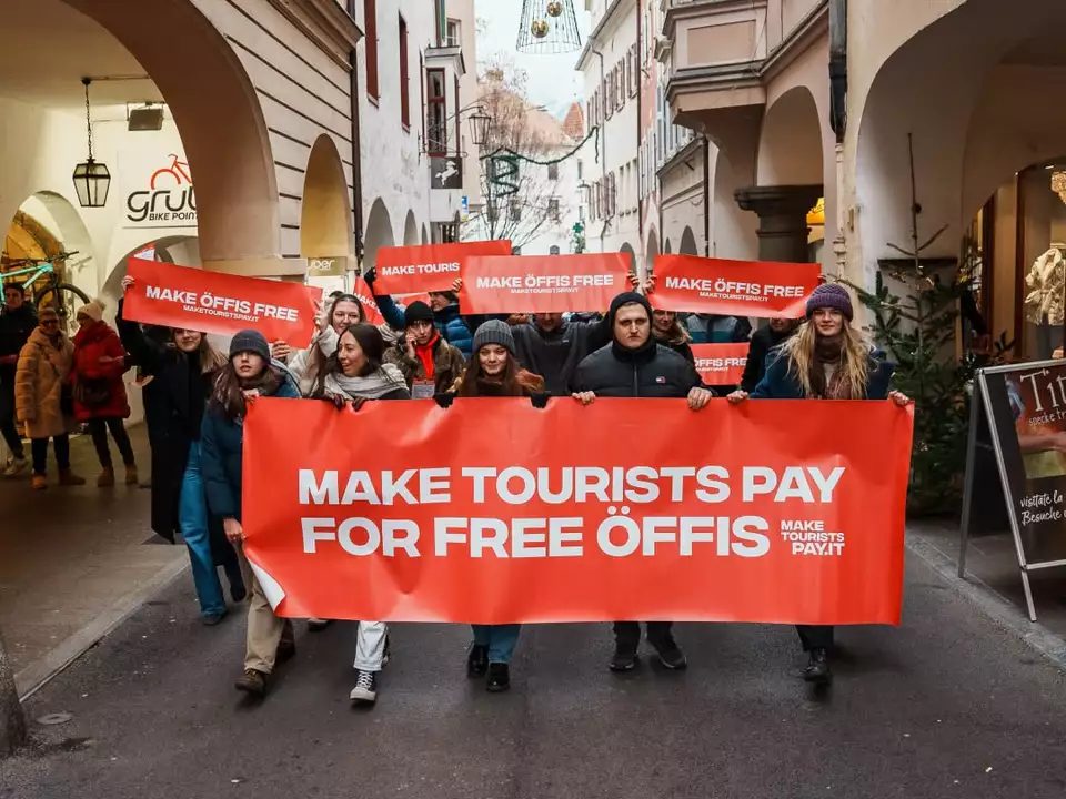 Demonstrierende mit rotem Banner „Make Tourists Pay for Free Öffis“ in den Bozner Lauben